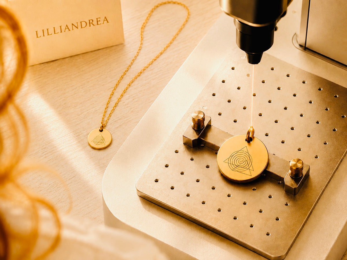 Gold LILLIANDREA harmony symbol pendant during laser engraving, with the matching necklace beside it.